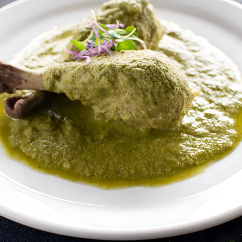 Two chicken drumsticks covered in a vibrant green mole sauce, garnished with microgreens.