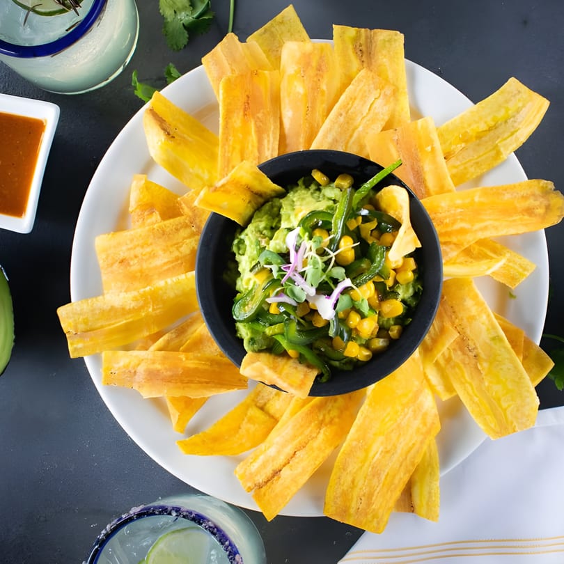 Guacamole with corn and peppers, surrounded by plantain chips, salsa, and a margarita.