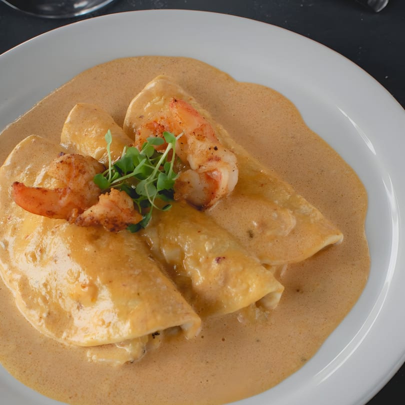 Three shrimp enchiladas covered in a creamy sauce, garnished with microgreens, on a white plate.